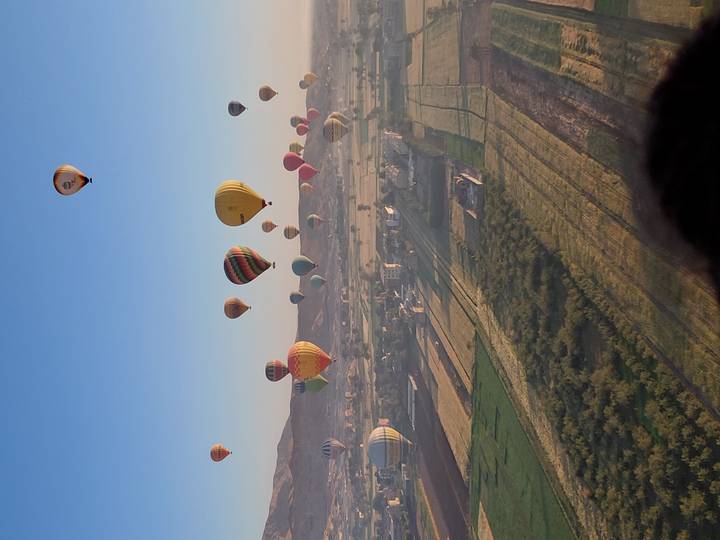 Dozens of colorful hot-air balloons drifting over patchwork fields at sunrise near the Nile in Luxor