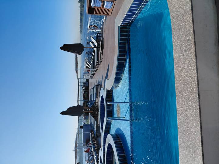 Sunny upper deck of a Nile cruise ship featuring tiered blue-tiled swimming pools and loungers overlooking the river