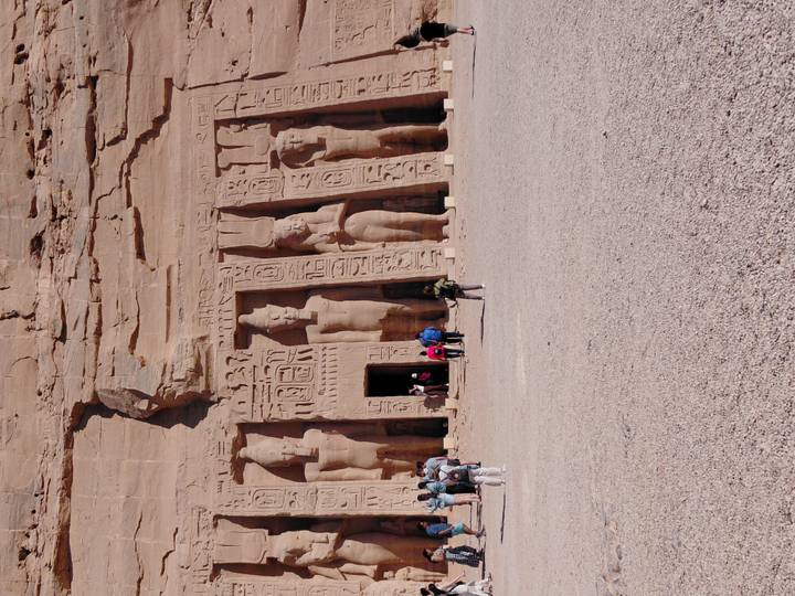 Carved statues on the facade of the Small Temple at Abu Simbel with tourists approaching across open ground