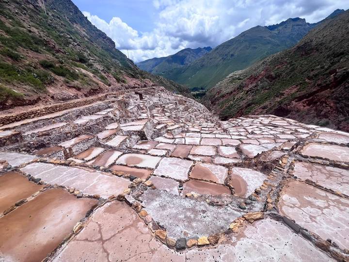 Close-up perspective of the geometric pink-hued evaporation ponds at the Maras salt mines against green mountains.