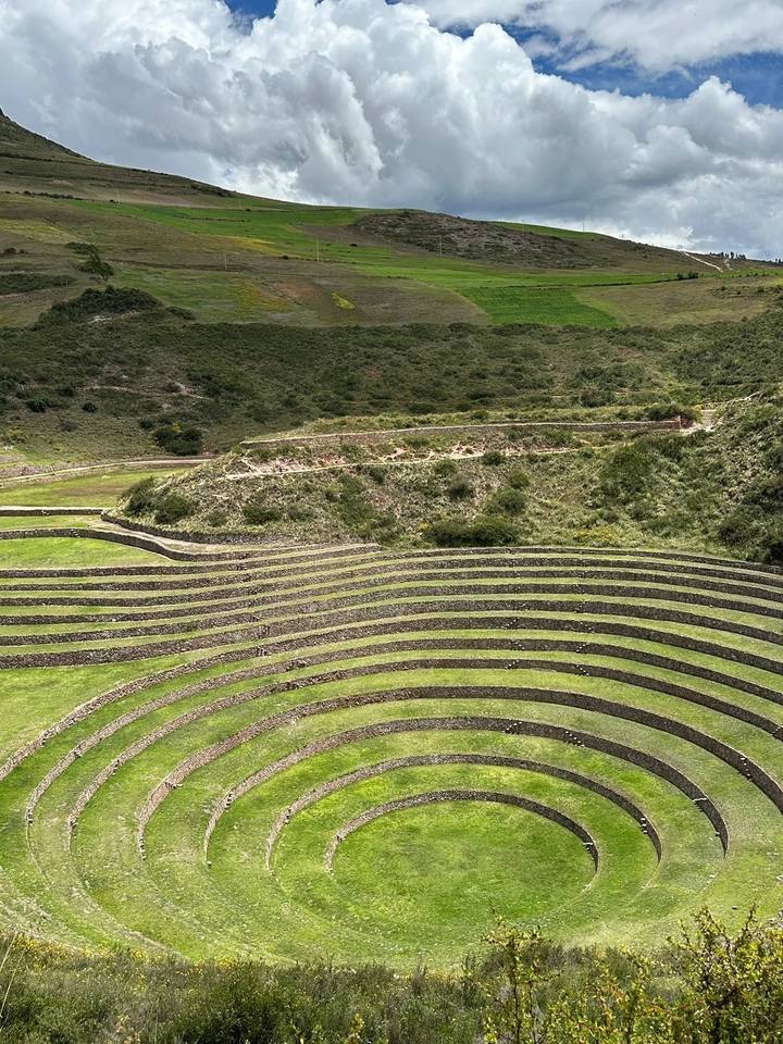 Terraced circles of Moray carve across a green hillside creating rhythmic contours.
