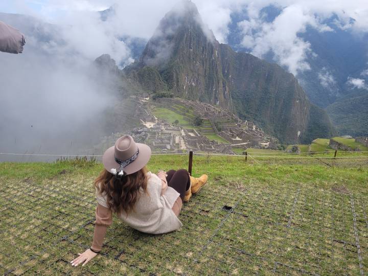 A traveler lounges on the grass gazing at Machu Picchu as clouds swirl around the mountain citadel.