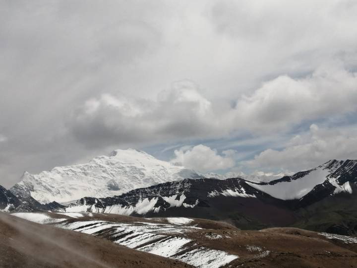 Snow-covered Andean massif rises above rolling foothills under a cloudy sky.