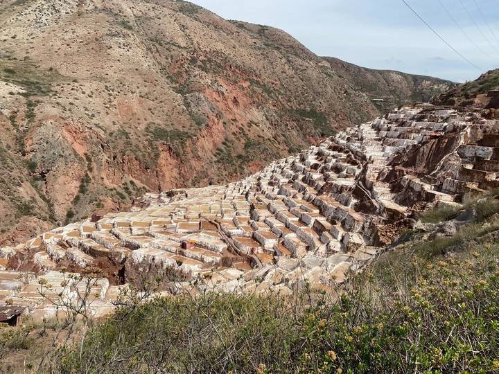 Tiered salt ponds cascade down a red rock ravine at Maras under a clear sky.