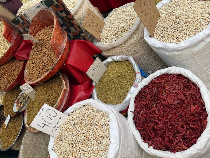 Colorful market stall with sacks of spices, dried chilies, pulses and nuts marked with handwritten price signs.