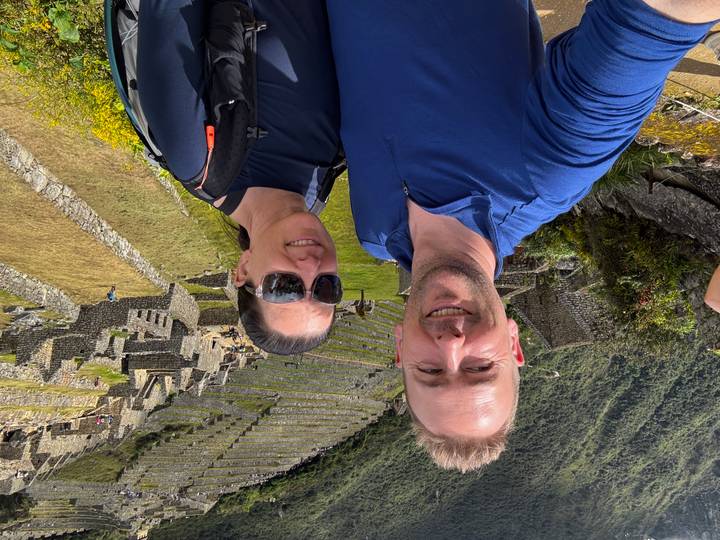 Couple in front of the stone terraces and lush slopes of Machu Picchu on a bright day.