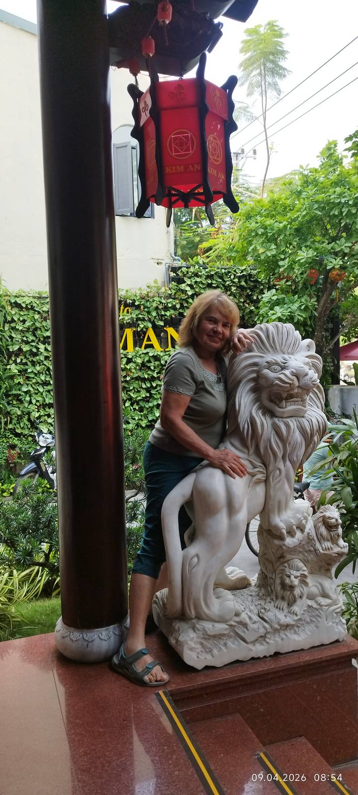 Woman posing beside a carved marble lion statue in a leafy courtyard