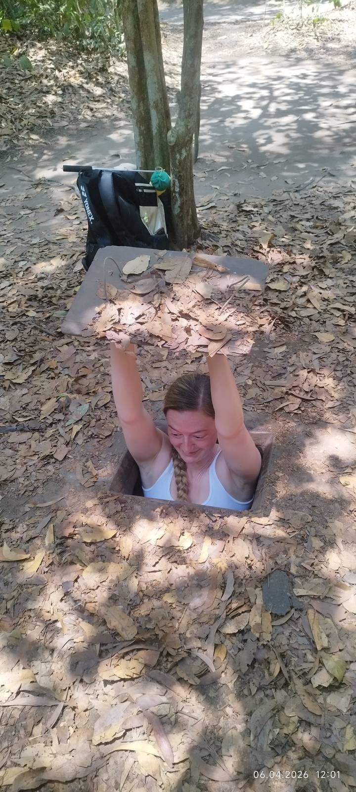 Woman emerging from a narrow Cu Chi tunnel holding a camouflaged lid above her head