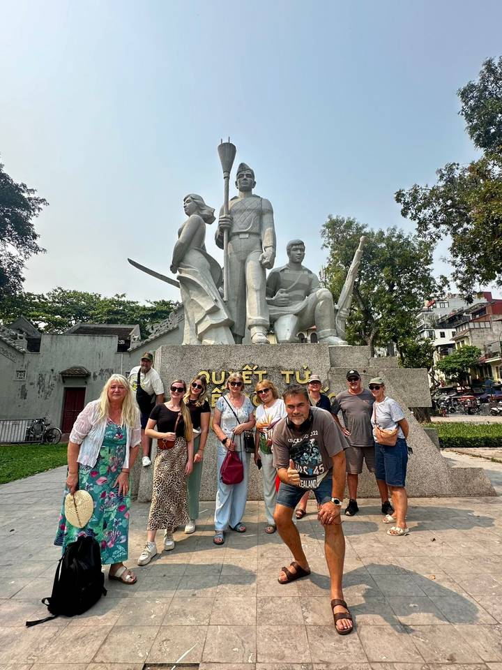 Group posing before a large patriotic statue in a Hanoi park