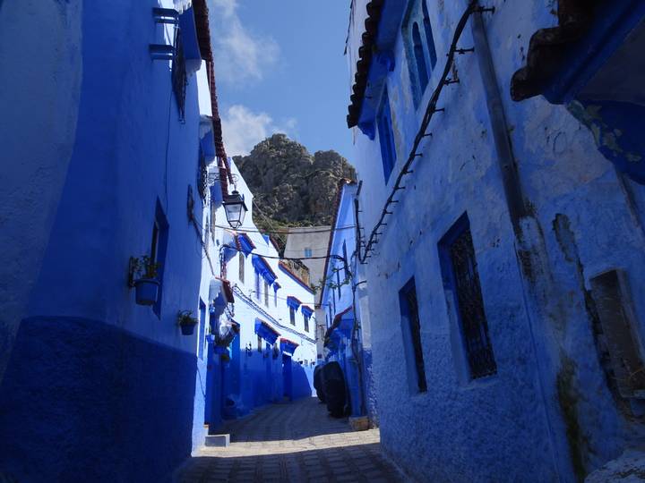Narrow alley of blue-painted houses in Chefchaouen with mountain peak framed above