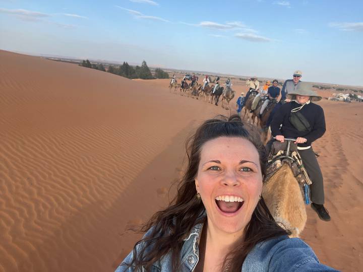 Selfie of excited traveller leading a long camel caravan across Sahara dunes