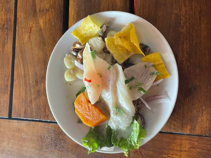 Plate of Peruvian ceviche with fish, sweet potato, corn and plantain chips on a wooden table