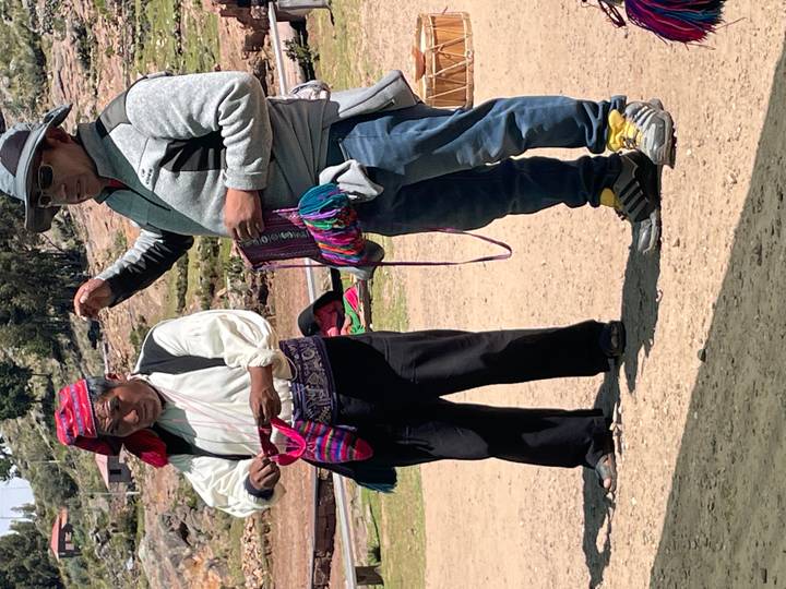 Two men in traditional attire display hand-woven pouches during an outdoor craft presentation