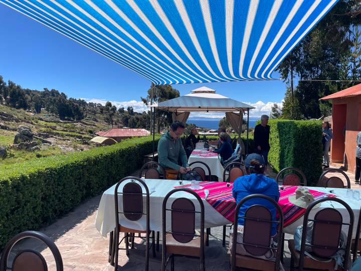 Outdoor patio with tables covered in colorful cloths where travelers gather beneath a striped canopy