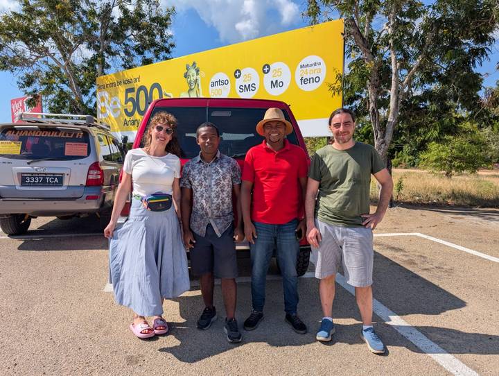 Four travelers pose in front of 4x4 vehicles on a sunny roadside.
