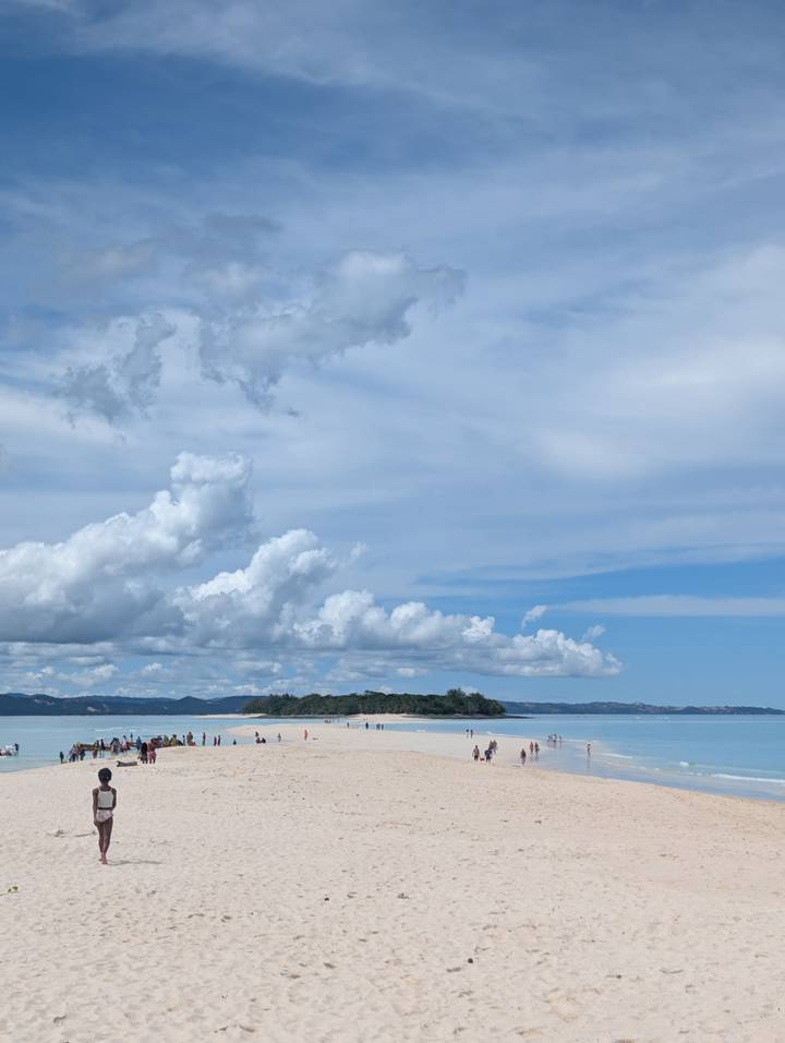 Wide view of a small green island beneath dramatic clouds and blue sky over calm ocean.
