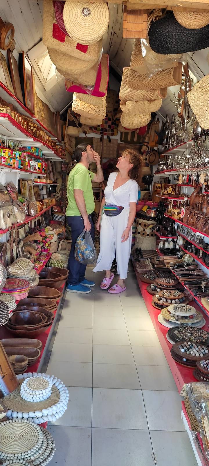 Two travelers browse colorful handicrafts and souvenirs inside a market stall.