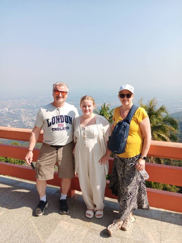Family of three posing at mountain viewpoint above sprawling city landscape.