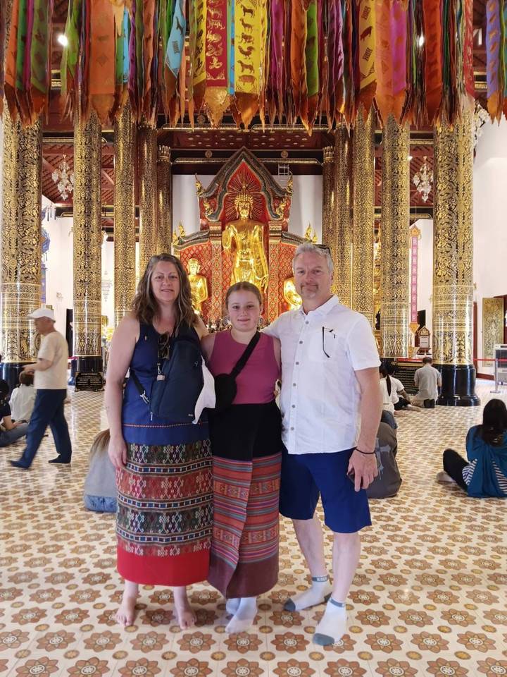 Family posing inside ornate Thai temple with golden Buddha statues and tall gilded columns.
