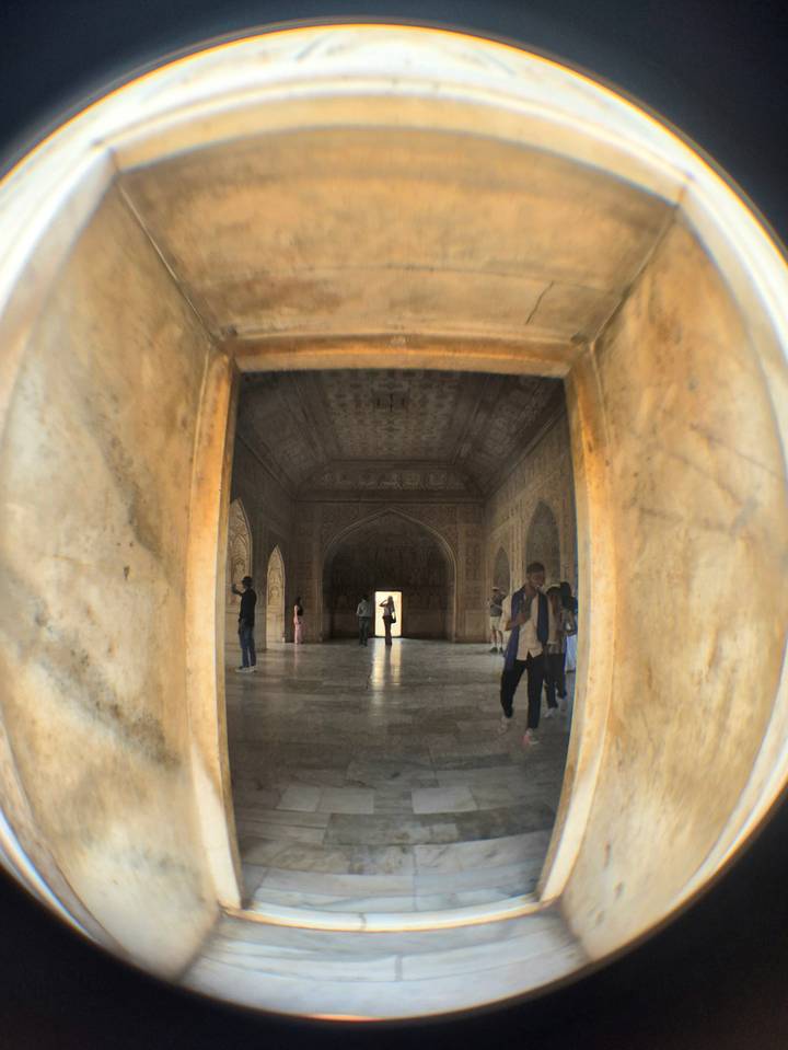 Visitors explore a dimly lit Mughal-era hall with carved arches and faded wall patterns.