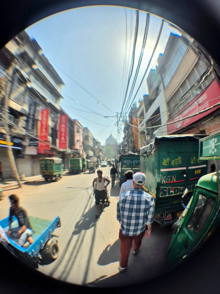 Bustling Old Delhi street with rickshaws, electric wires overhead, and distant Mughal dome visible.