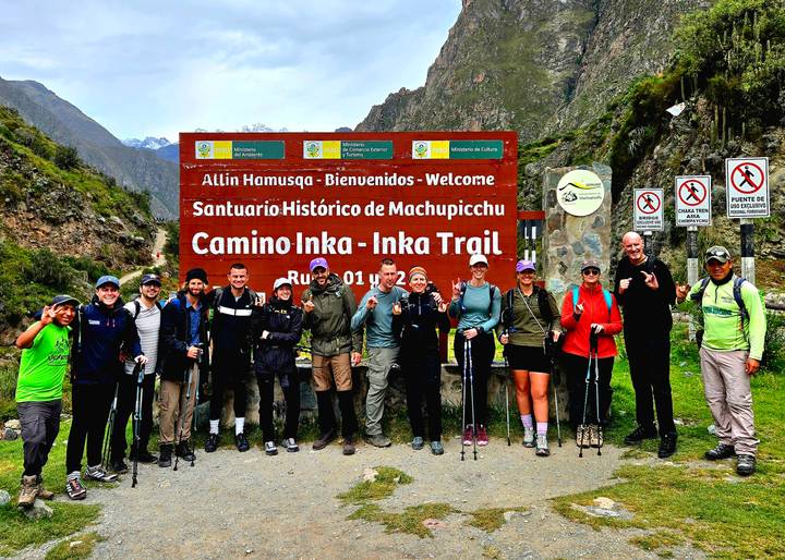 Excited trekking group posing by the Camino Inka trailhead welcome sign