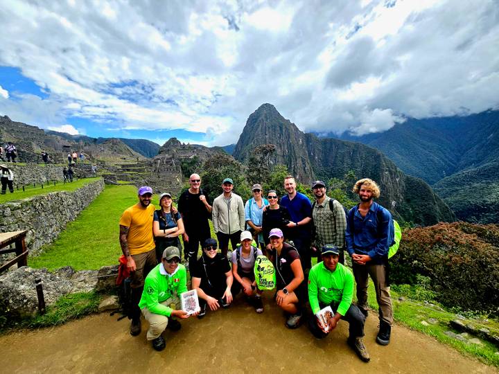 Tour group smiling for a photo on grassy terraces with Machu Picchu in the background