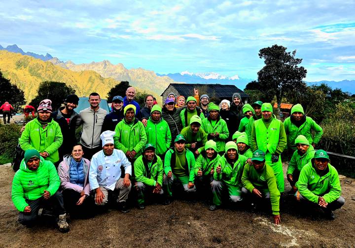 Large team of porters in matching green jackets posing together at camp