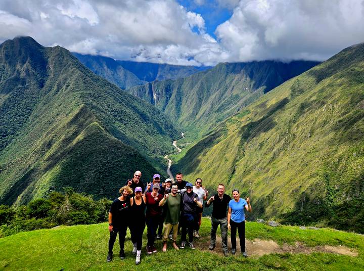 Trekkers celebrating on grassy lookout with sweeping valley and river below