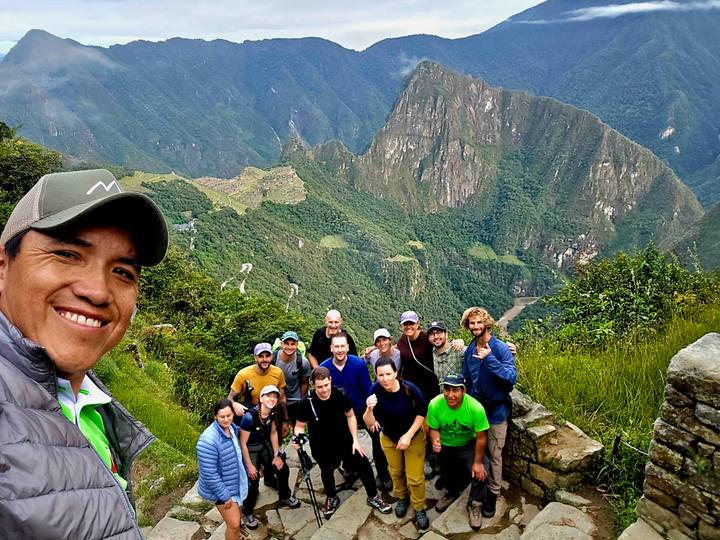 Selfie of guide with group at scenic overlook of Machu Picchu ruins far below