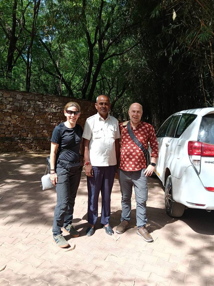 Two tourists posing with their driver beside a white vehicle on a shaded paved path