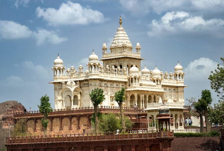 Elegant white marble cenotaph with domes and intricate carvings standing against a blue sky