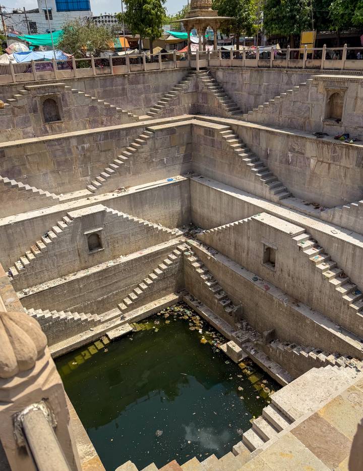 Geometric stone stepwell with steep zig-zag staircases descending to murky water below