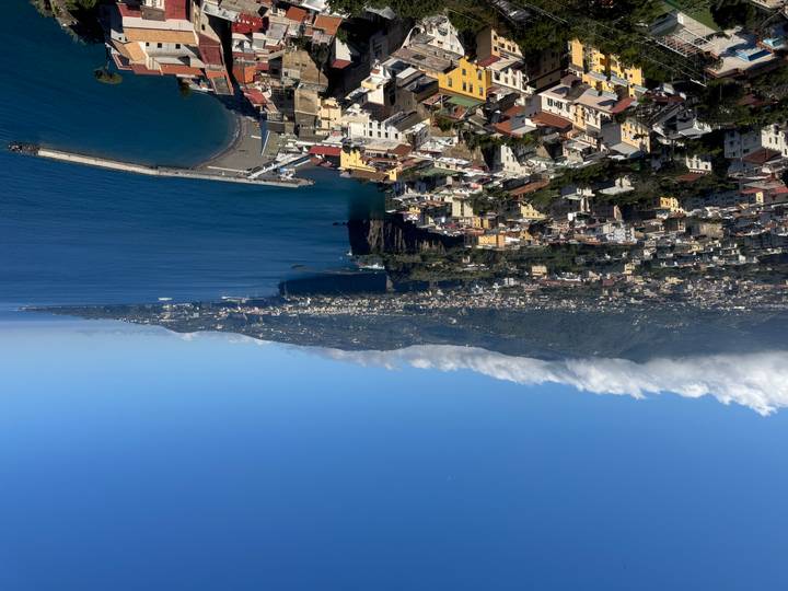 Panoramic overlook of Sorrento coastline with town rooftops, cliffs and sweeping blue bay under clear skies.
