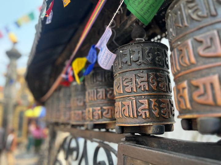 Close-up of bronze Tibetan prayer wheels with decorative script at a Buddhist site.