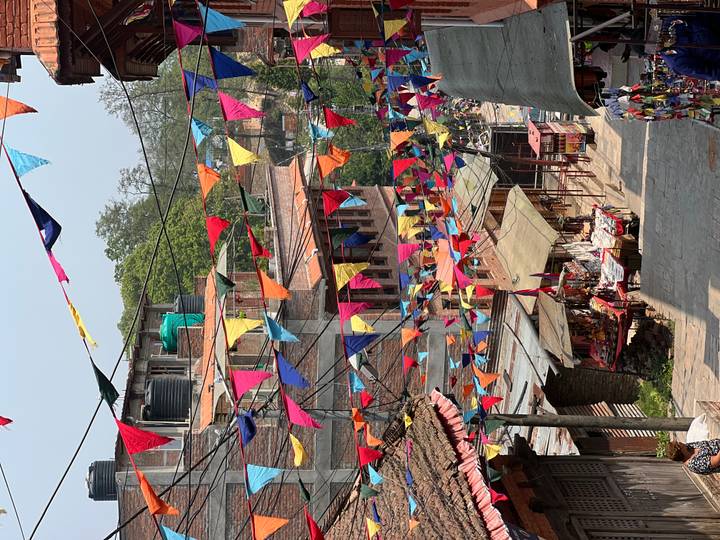 Narrow street draped with multicolored triangular flags and small market stalls below.