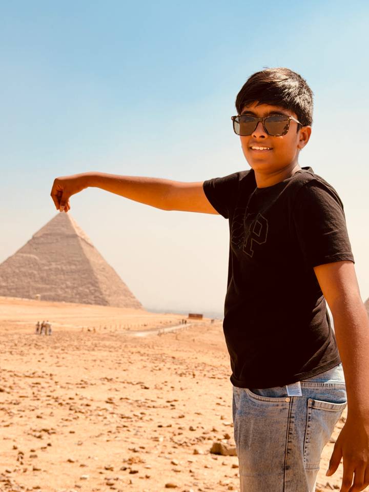 Boy pretending to hold pyramid between fingers against sandy expanse