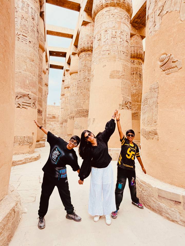 Family stretching arms playfully among massive columns of Karnak temple