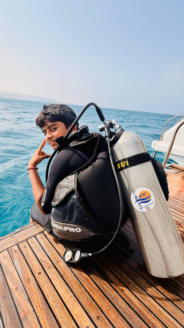 Young diver on boat preparing scuba tank, flashing peace sign over blue sea