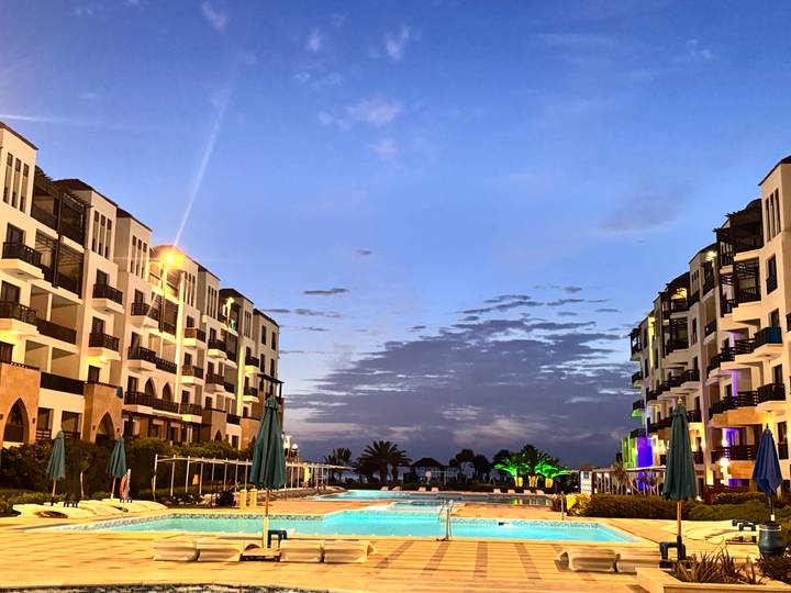 Resort pool flanked by modern white buildings against colourful dusk sky