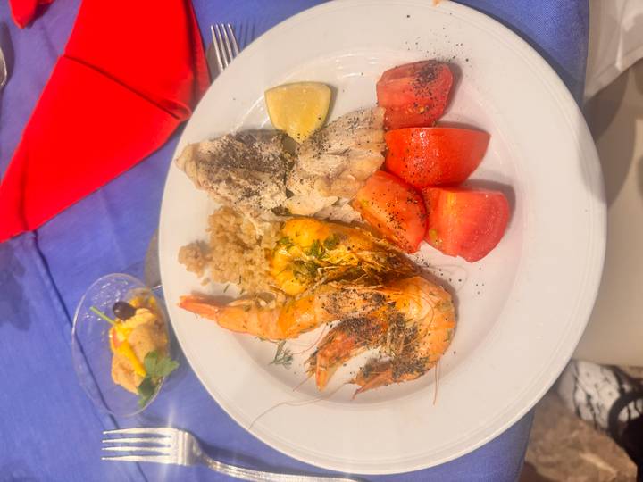 Dinner plate with prawns, fish, rice and tomatoes on restaurant table