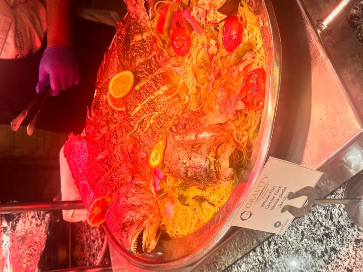 Large whole fish served over pasta at buffet under warm heat lamps