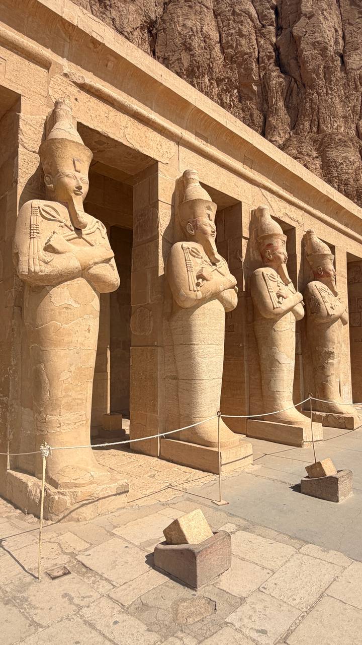 Row of colossal Osiride statues lining temple colonnade in bright desert sun