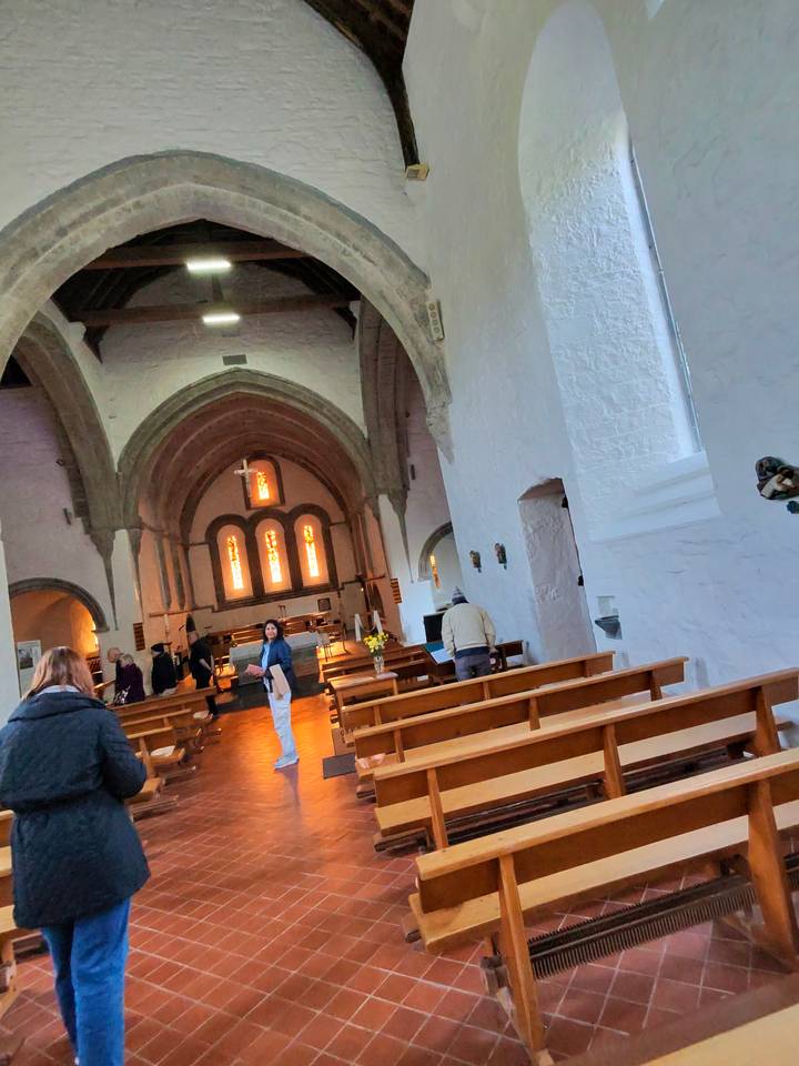 Interior of a small stone church with vaulted arches and warm stained-glass windows during a visit.