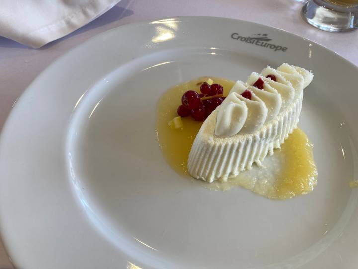 Plated gourmet dessert of creamy mousse topped with red currants and drizzled sauce on a white plate.