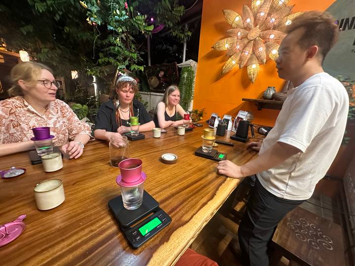 Participants seated at a wooden bar learning about Vietnamese coffee preparation with colorful drip filters.