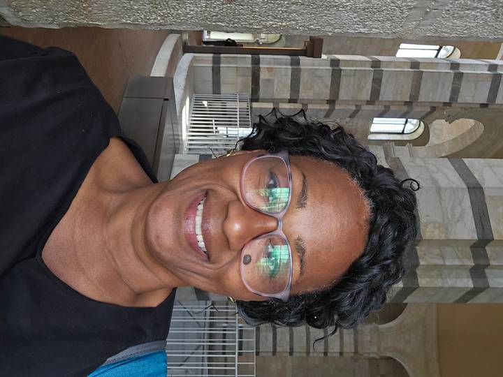 Smiling woman wearing glasses taking a selfie inside a marble-columned historic building.
