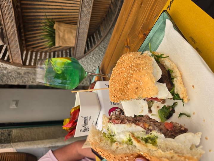 Sesame burger with melted cheese on a tray, green cocktail in background