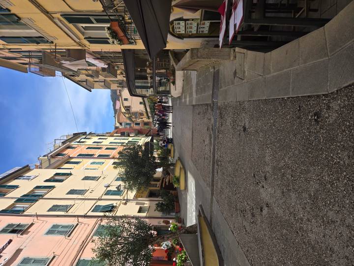 Upward sloping street lined with pastel buildings and shops in a Cinque Terre village