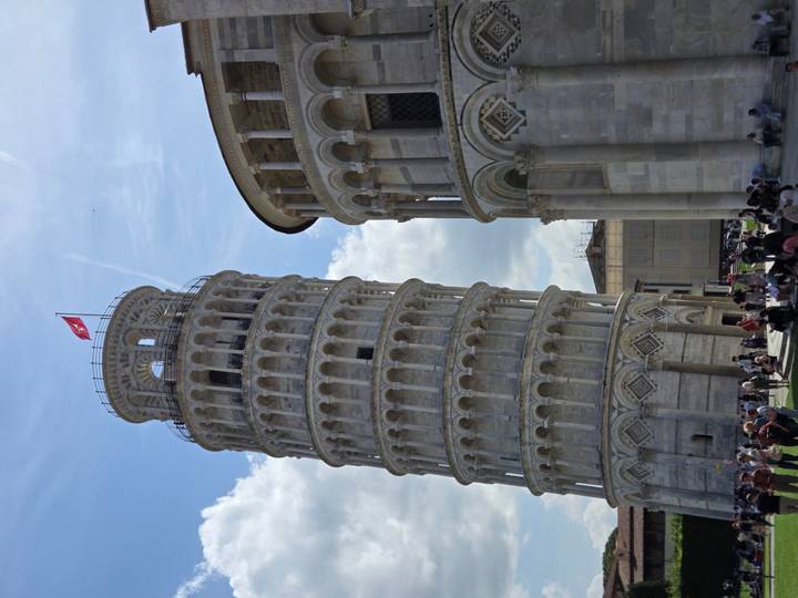 Leaning Tower of Pisa beside Pisa Cathedral under partly cloudy sky with crowds below